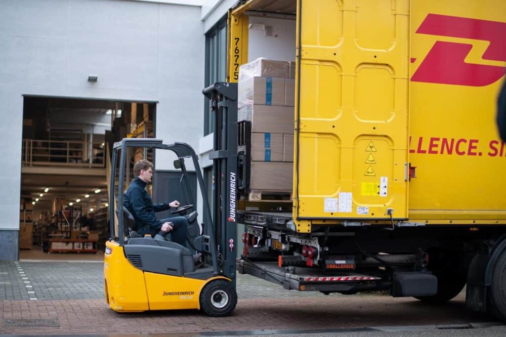 Mann lädt Paket mit Gabelstapler in gelben DHL LKW